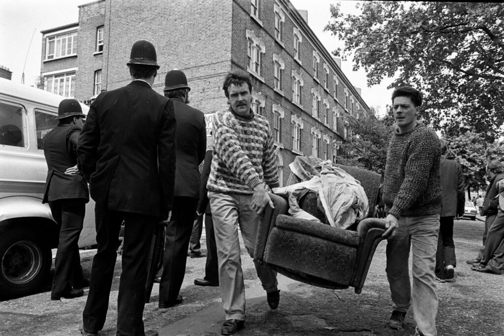 Men carrying armchair through street following eviction by police